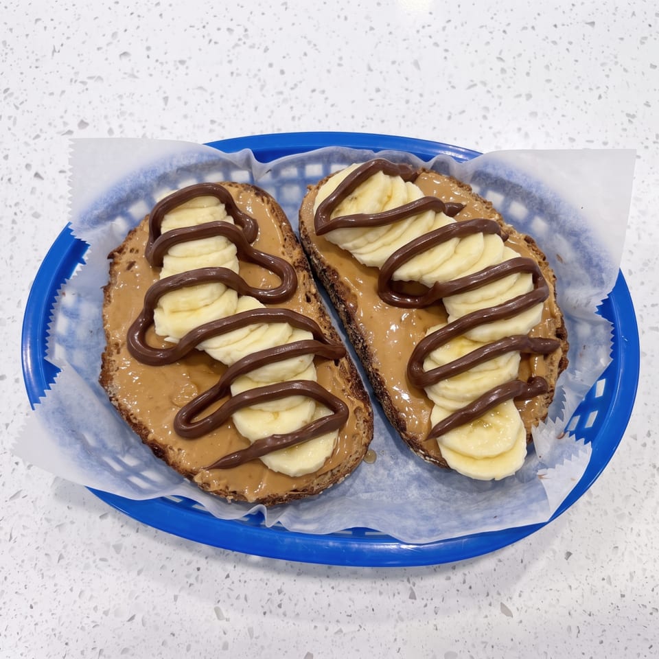 Two slices of toast topped with peanut butter, banana slices, and chocolate drizzle on a blue plate.