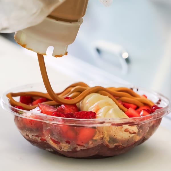 Chocolate-covered strawberries and bananas in a clear dessert bowl, with chocolate sauce being poured over the fruit.