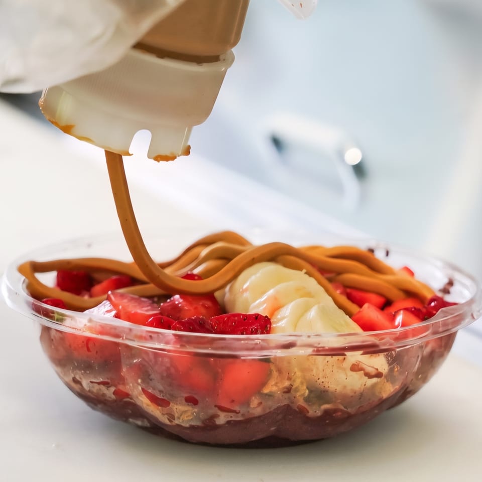 Chocolate-covered strawberries and bananas in a clear dessert bowl, with chocolate sauce being poured over the fruit.