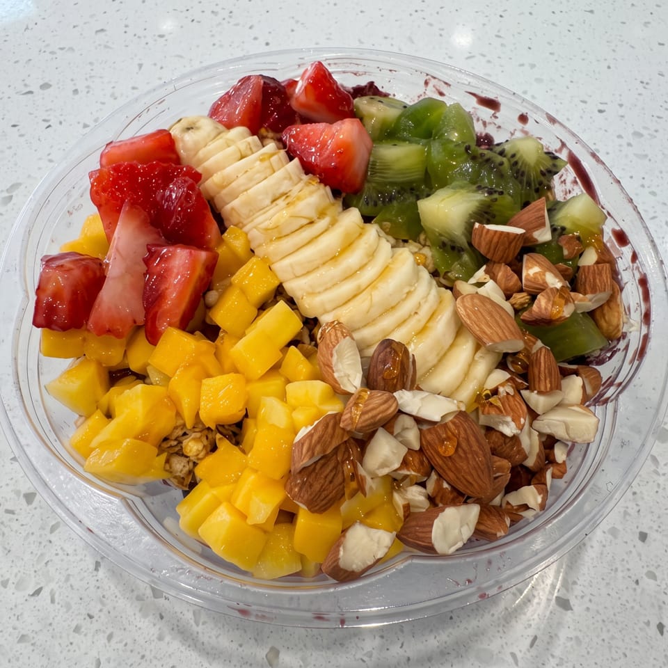 Colorful fruit bowl with strawberries, bananas, kiwi, mango, and almonds on a white speckled counter.